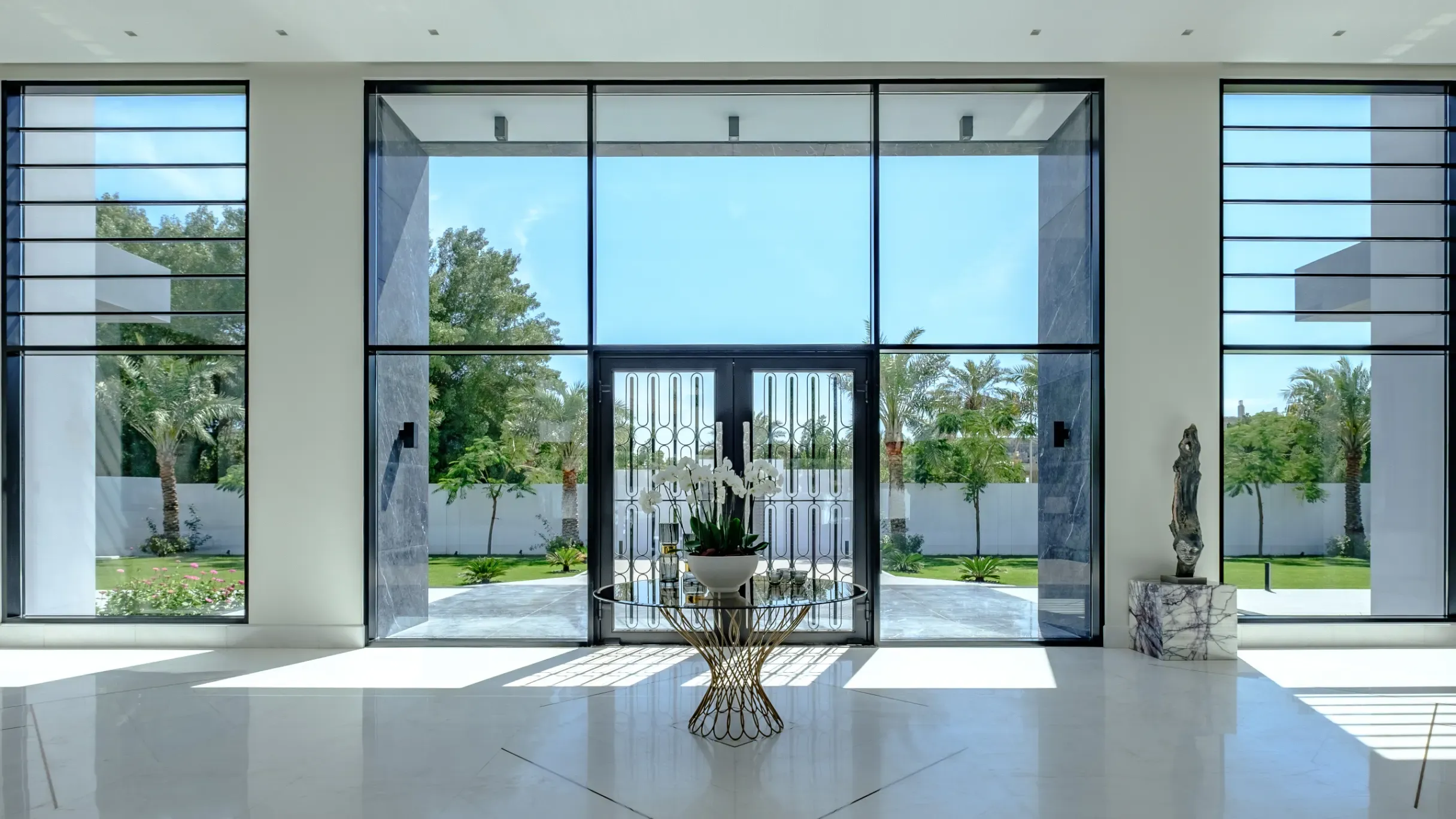 Luxury villa entrance in Hamala, Bahrain, with white marble flooring, dark accents, and floor-to-ceiling garden views.