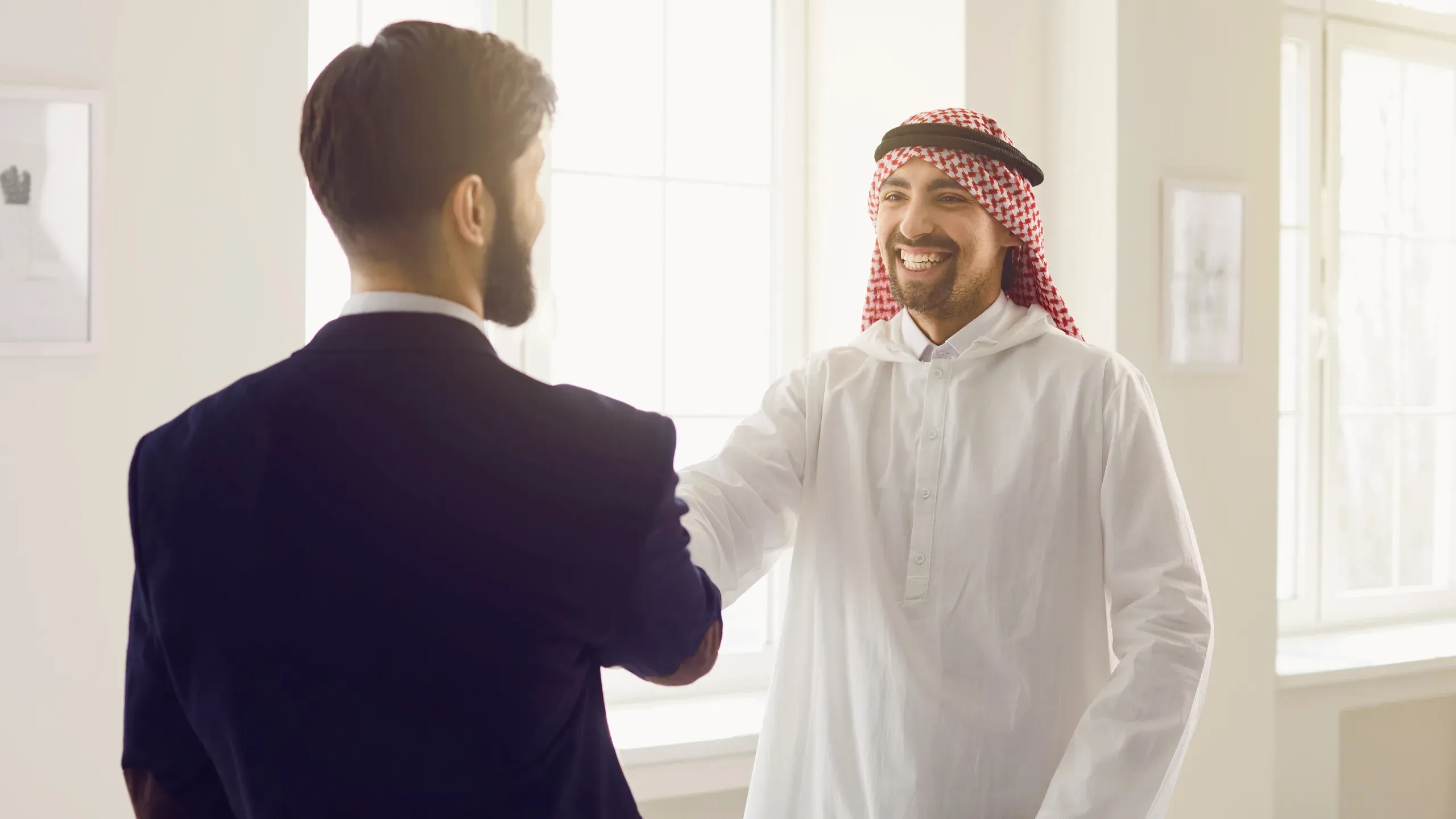 European and Arabic businessmen shaking hands in an office, symbolising a successful Manama real estate agreement.