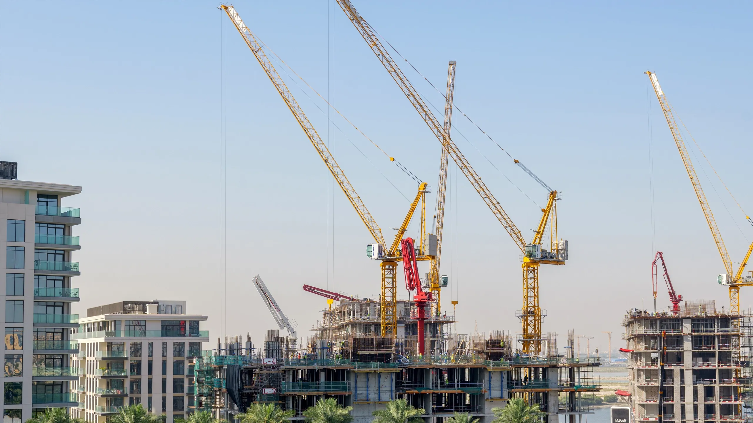 Active construction site featuring multiple tower cranes lifting materials for new high-rise building developments in Bahrain.