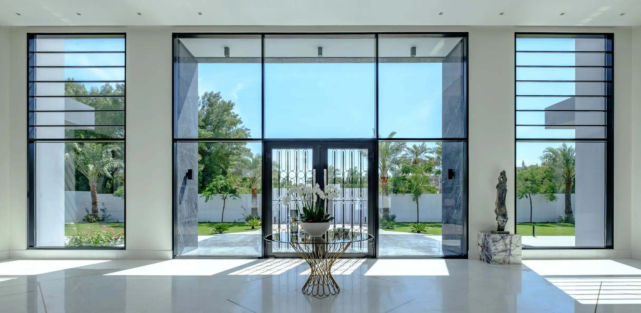 Luxury villa entrance in Hamala, Bahrain, with white marble flooring, dark accents, and floor-to-ceiling garden views.