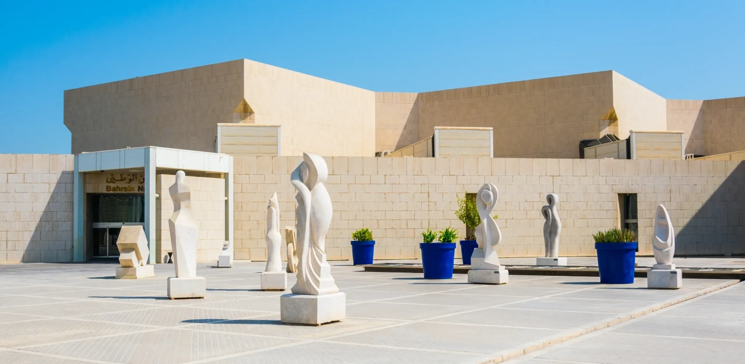 Bahrain National Museum waterfront exterior in Manama, featuring modern architecture and contemporary outdoor sculptures.