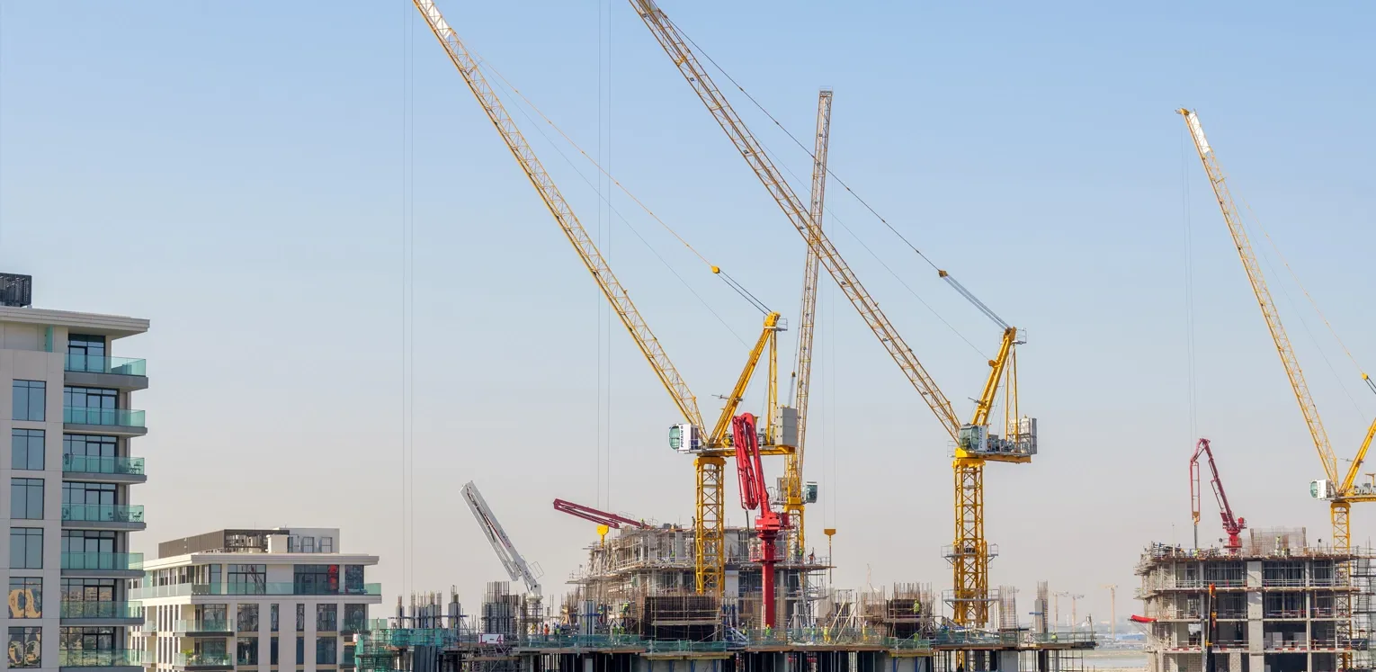 Active construction site featuring multiple tower cranes lifting materials for new high-rise building developments in Bahrain.